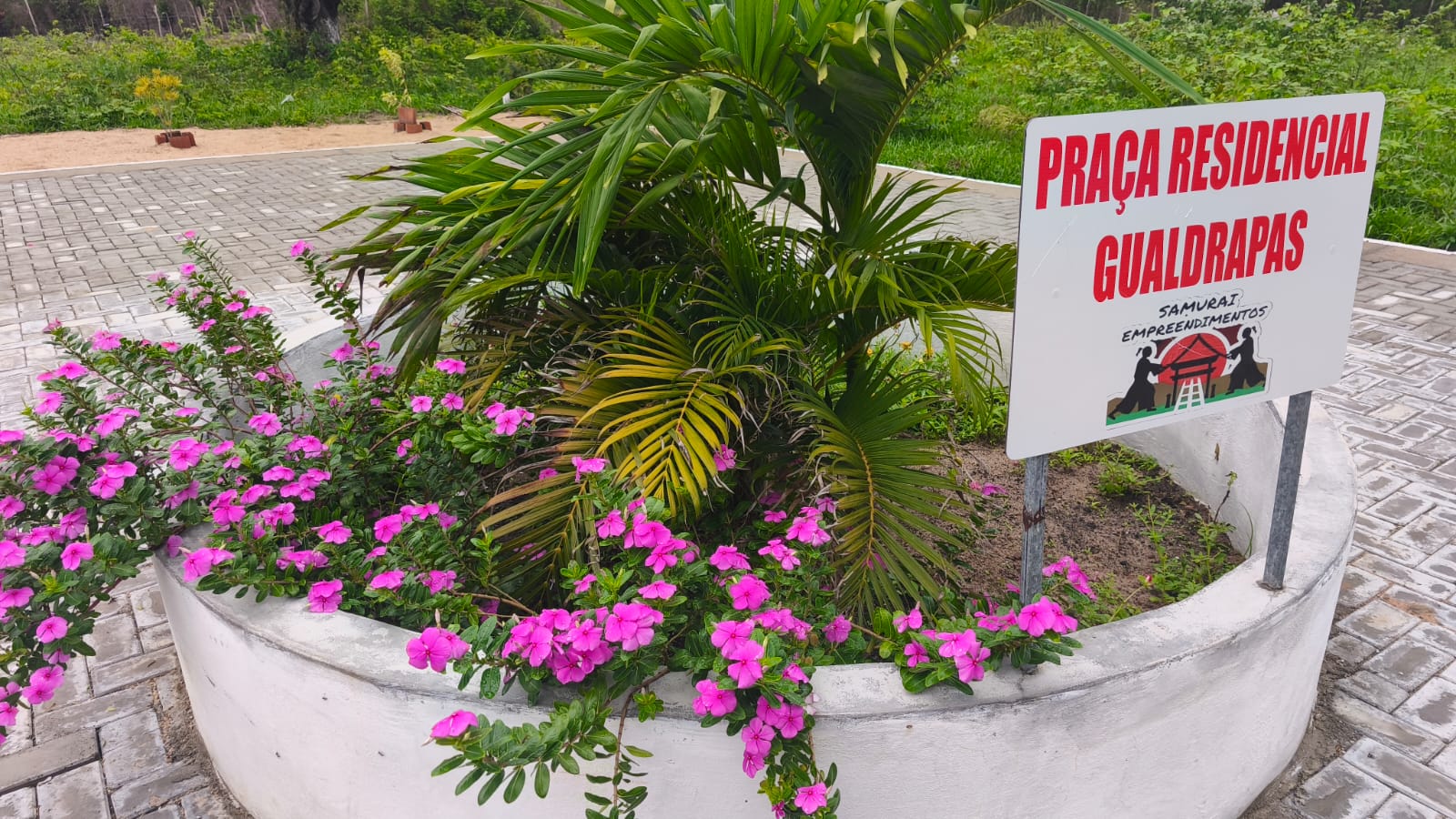 Praça do Residencial Gualdrapas com jardim florido e sinalização do empreendimento
